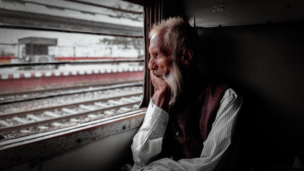 An old man looking through the window of a train