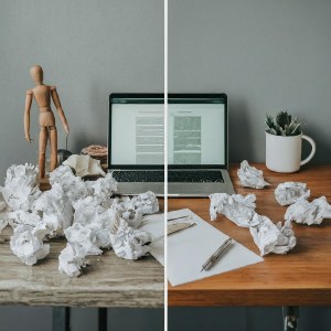 thrown papers in front of laptops on a table with a potted plant and doll 