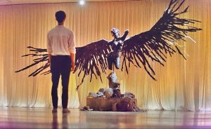 A man looking at a sculpture of an angel with broken wings 