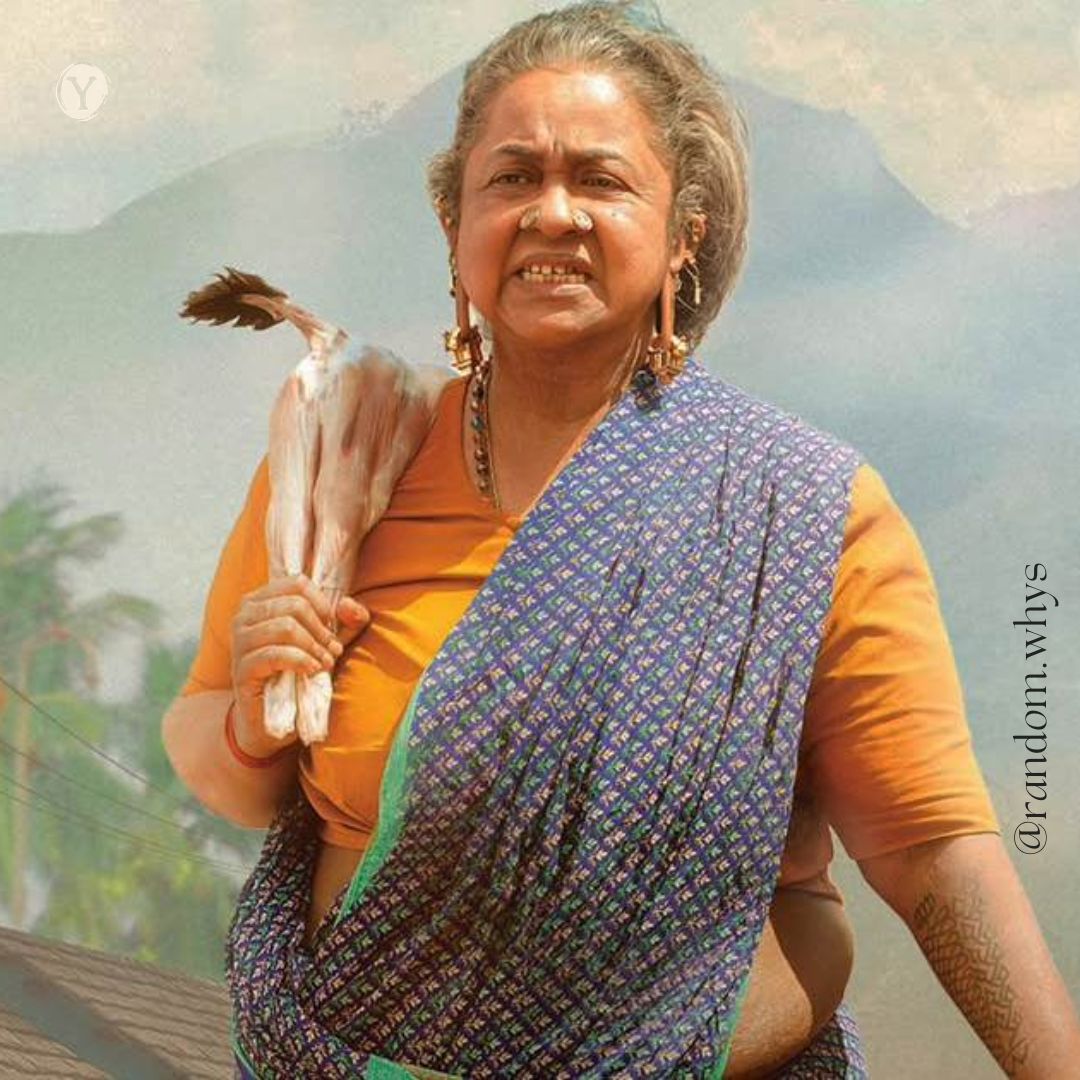 An elderly woman in a saree stands outdoors with a determined expression, holding a cloth bundle over her shoulder, with mountains blurred in the background.